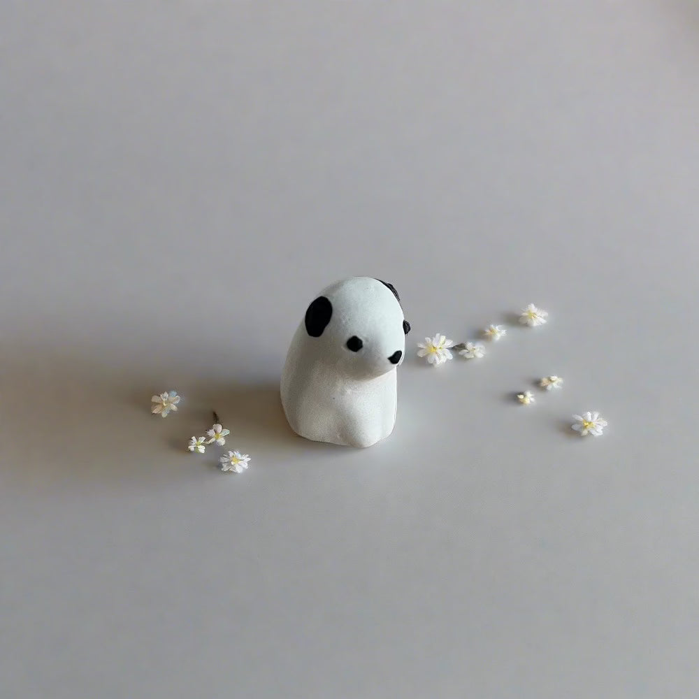 SÖPÖn pieni keraaminen valkoinen koira mustilla korvilla.