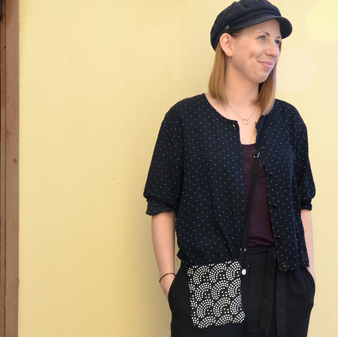 Mallin päällä Kui designin Helmi-pikkulaukku, Väri musta-valkoinen. Mallin takana keltainen tausta.