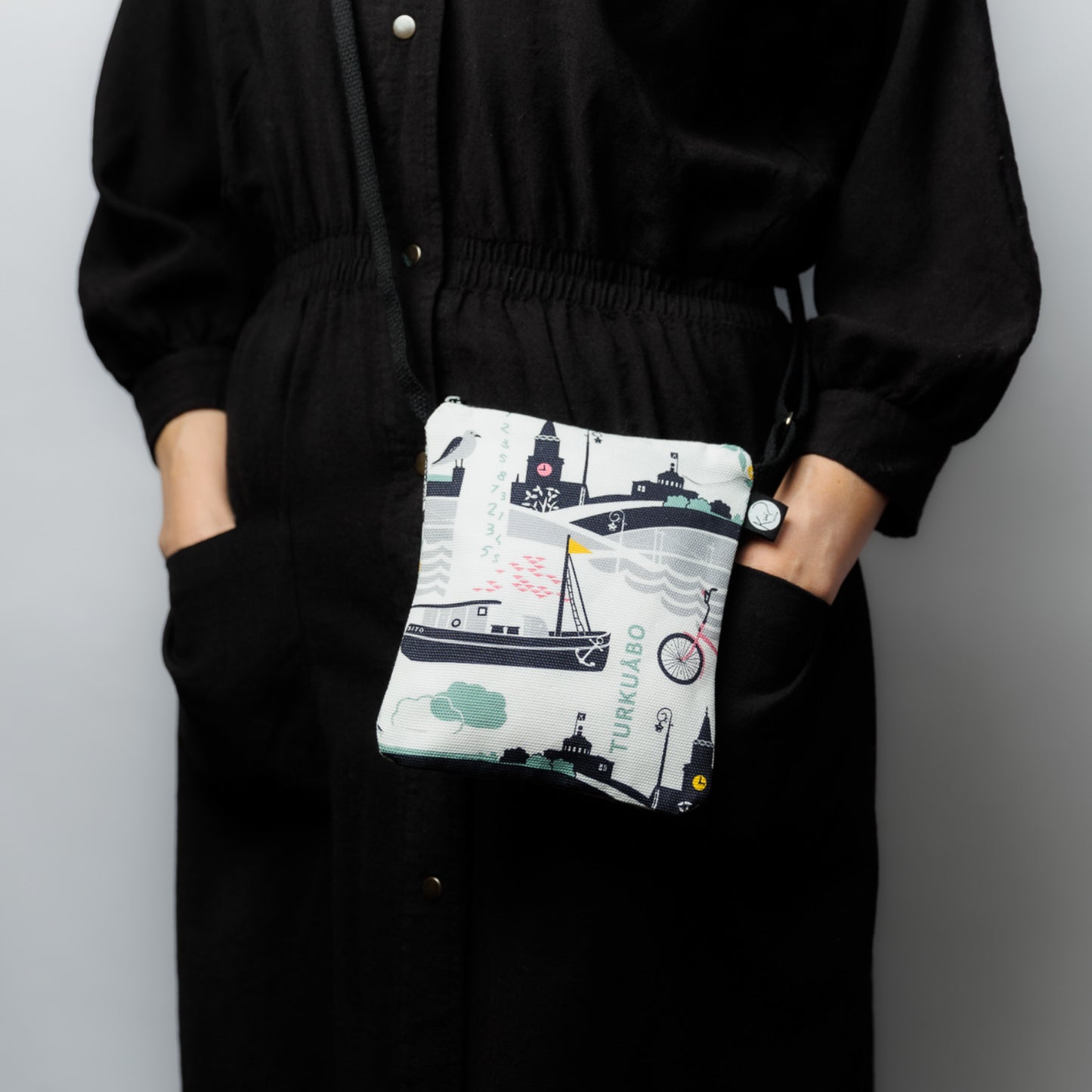 Mallin päällä Kui designin Tälpual ja toispual-pikkulaukku. Pohjaväri valkoinen, Roosan värisiä Turku-aiheisia kuvia.