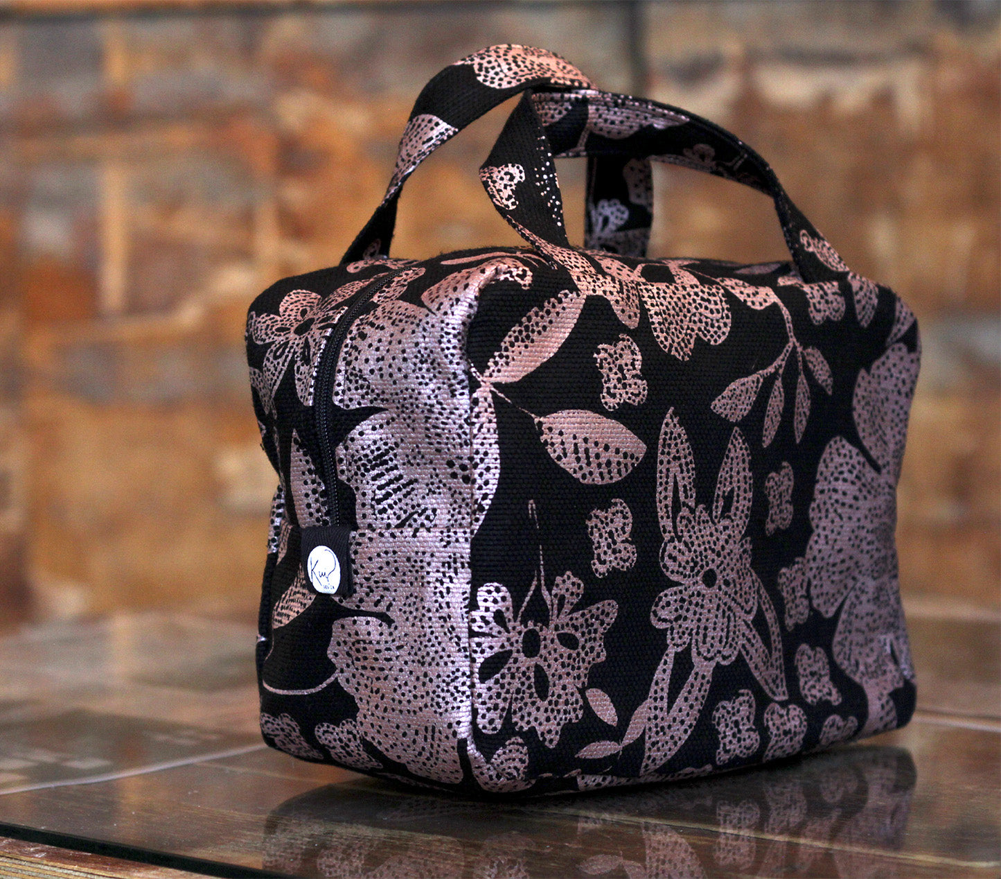 Kui designin Hulda-toilettilaukku. Musta pohjaväri, jossa kuparin värinen kukka kuosi.