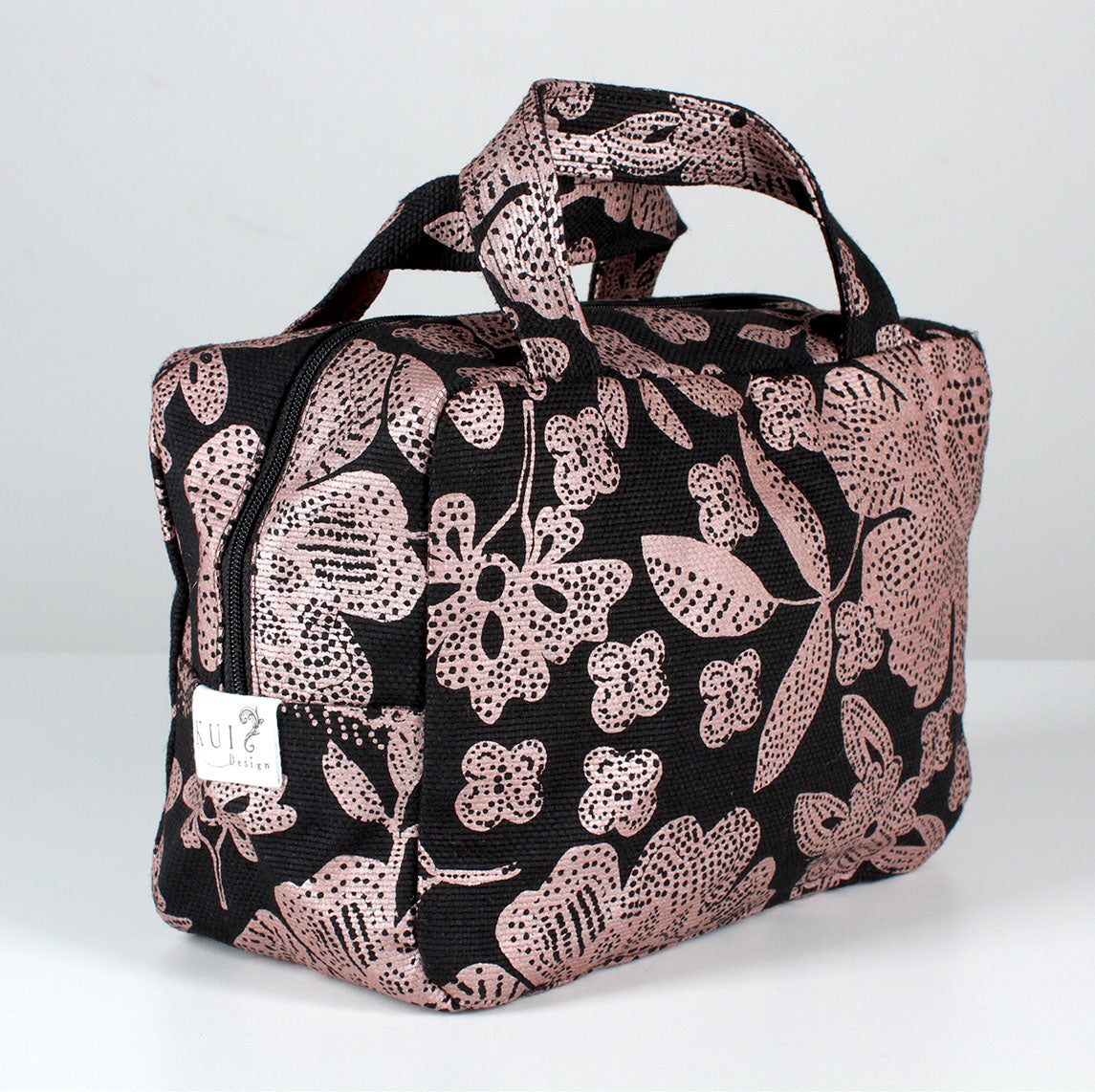 Kui designin Hulda-toilettilaukku. Musta pohjaväri, jossa kuparin värinen kukka kuosi.