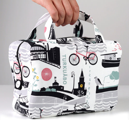 Kui designin Tälpal ja toispual-toilettilaukku. Valkoinen pohjaväri, jossa roosan värinen Turku-aiheinen kuosi.