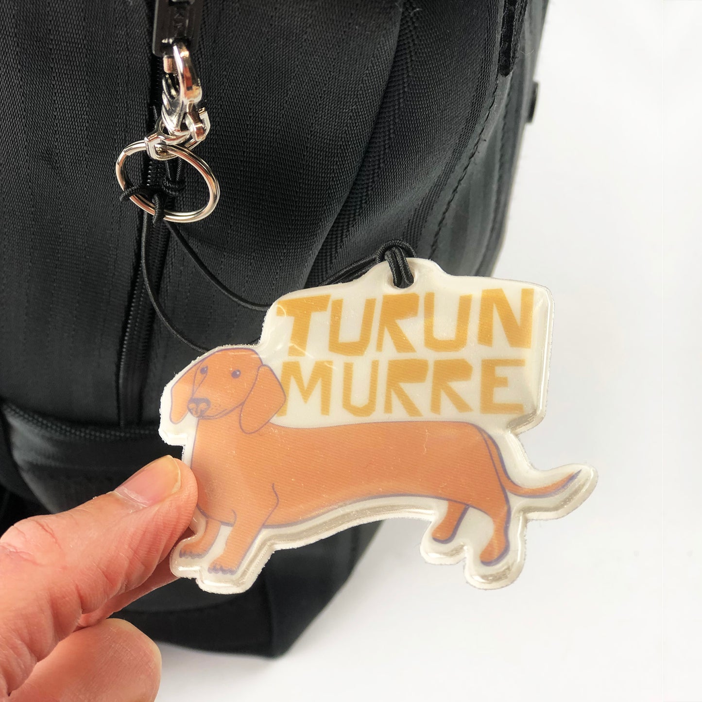 Kui designin Turun murre-heijastin kiinnitettynä laukkuun. Mäyräkoiran kuva.